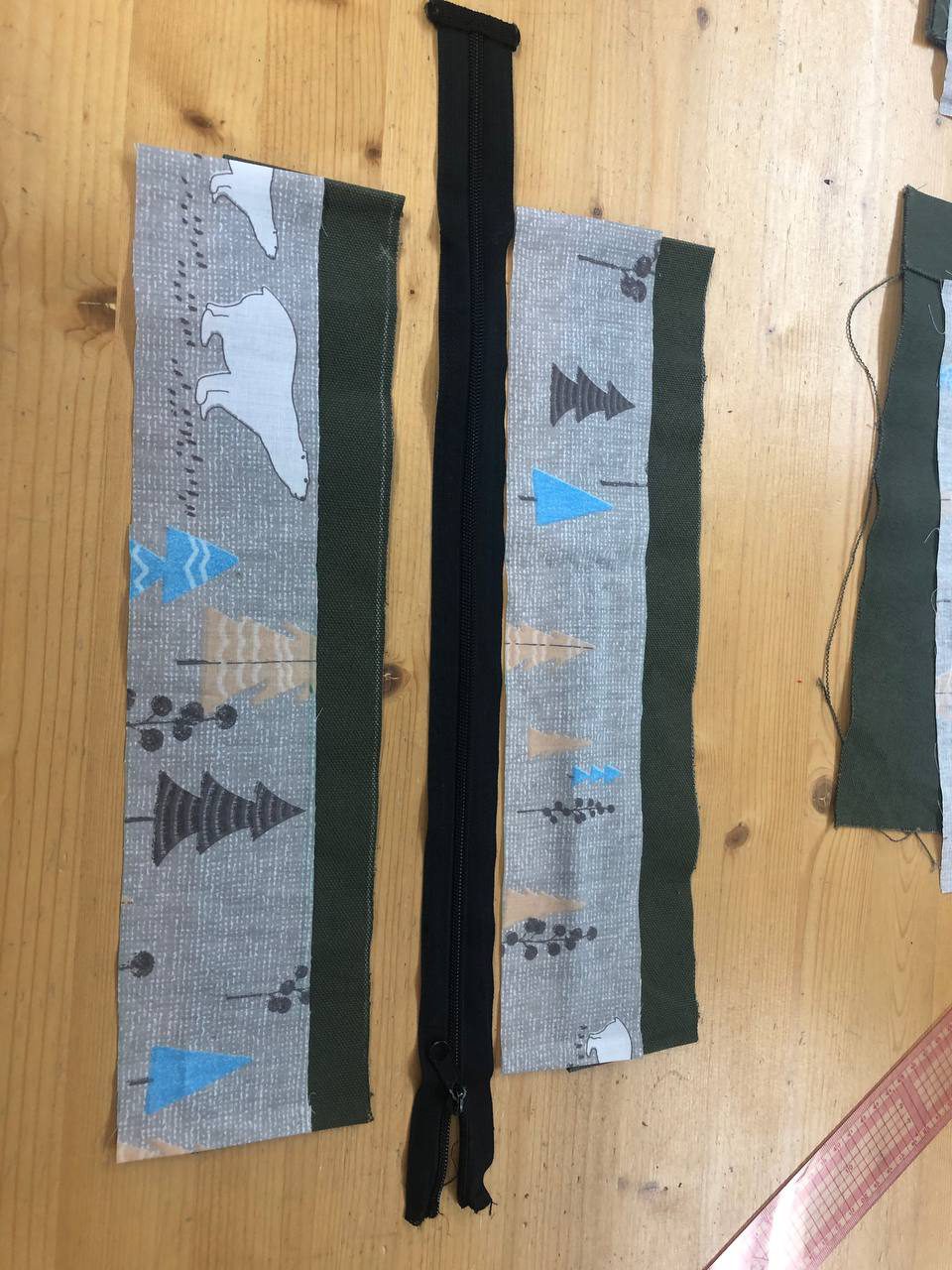 북극곰과 나무 무늬 안감, 카키색 겉감이 길게 재단되어 있고 가운데 검은 지퍼가 놓여 있다